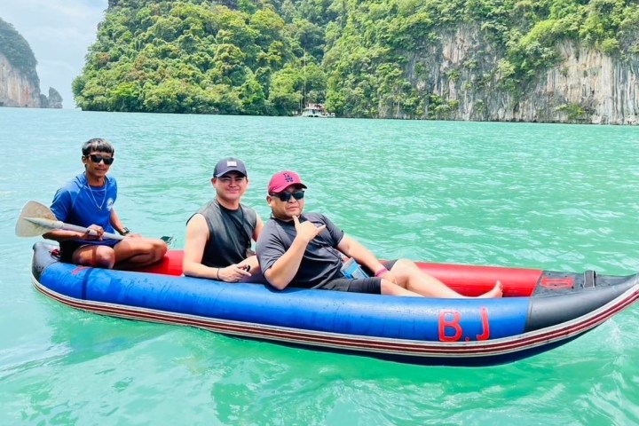Three people in an inflatable boat on turquoise water with green cliffs in the background.