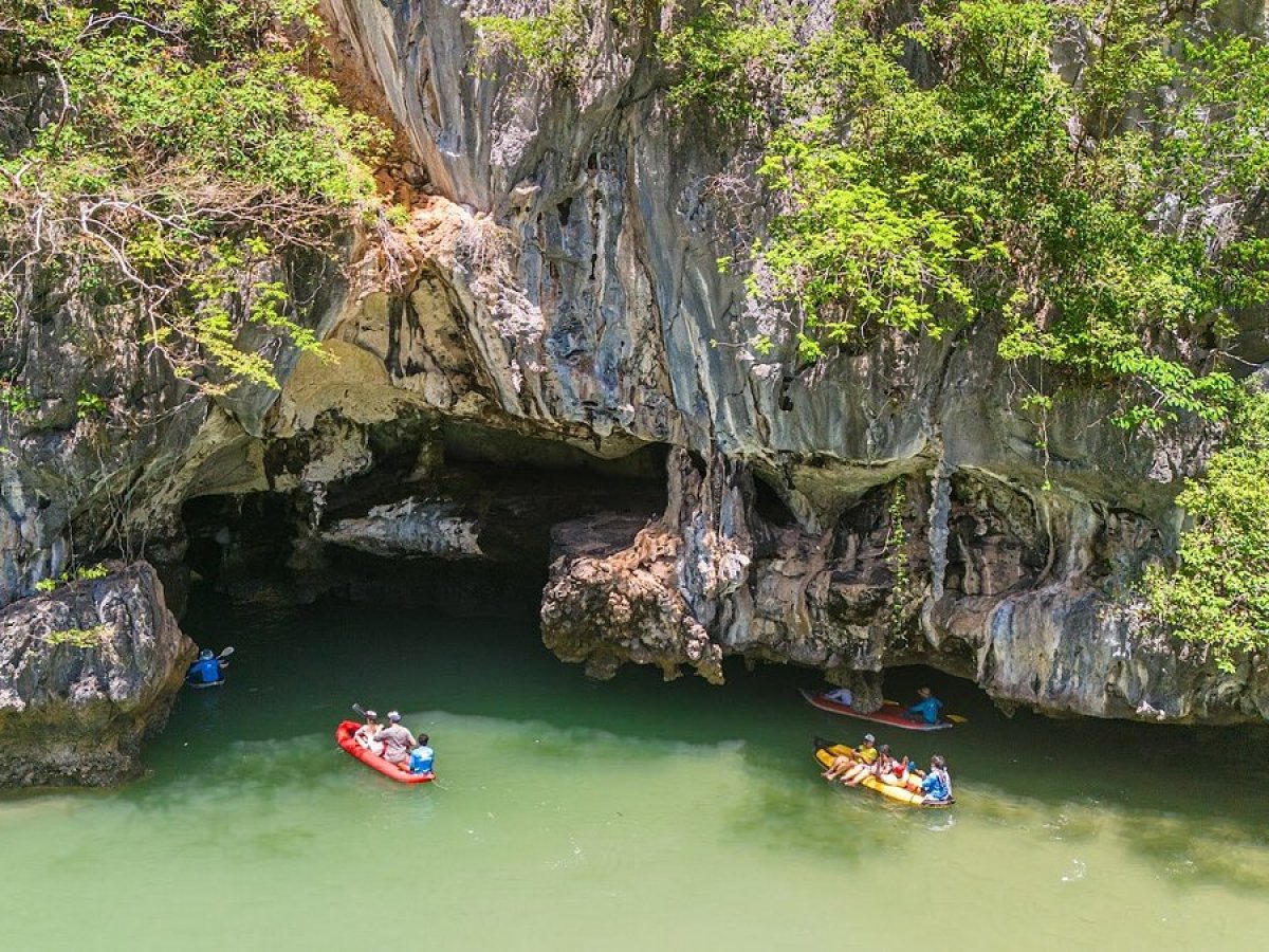 People kayaking near a cave entrance with lush greenery above.