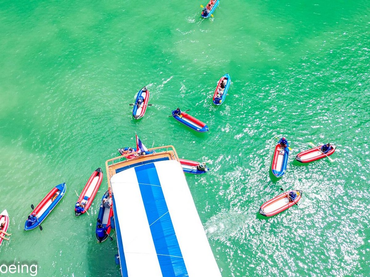 Aerial view of kayaks around a blue and white boat in clear green water.