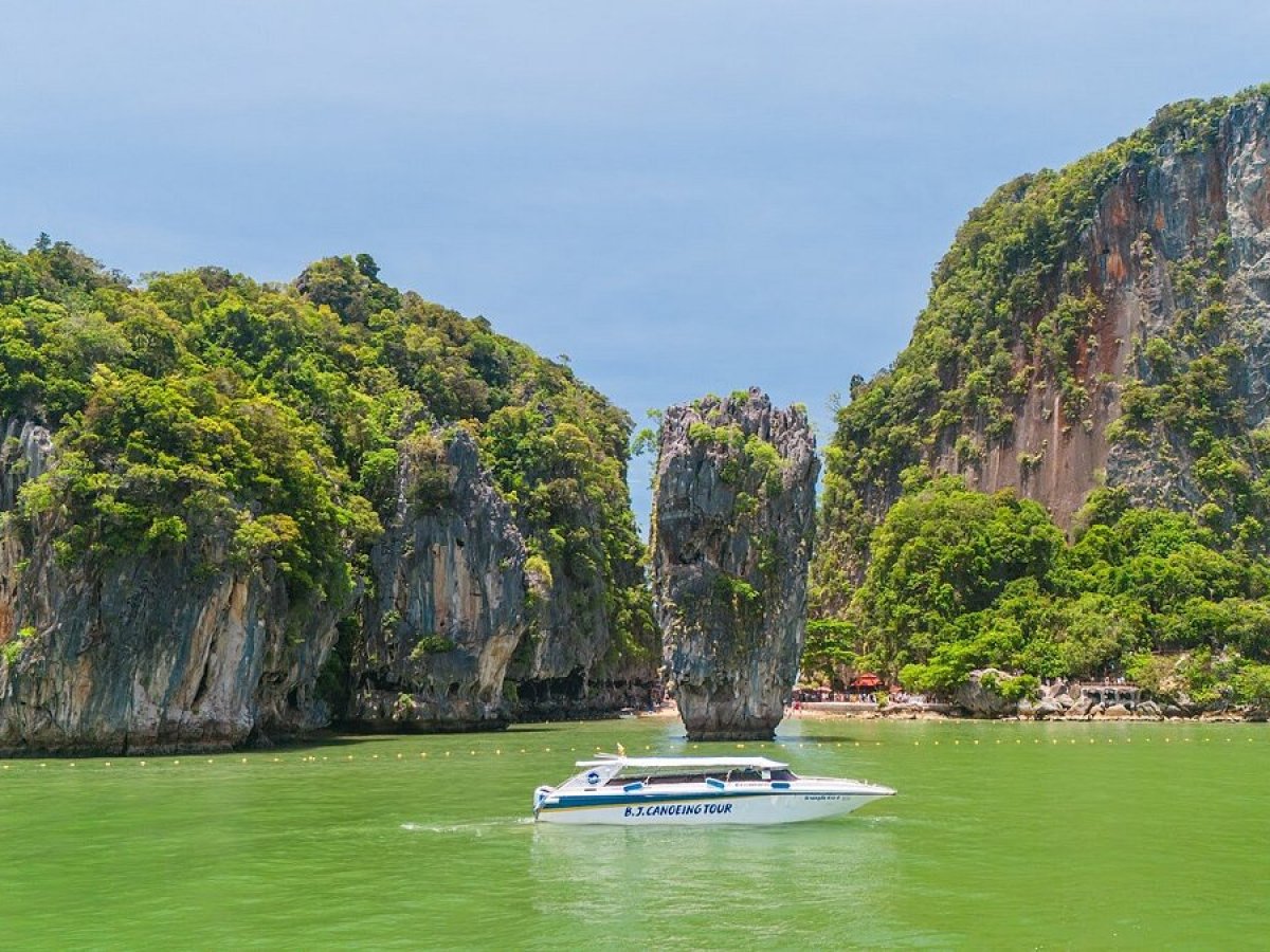 Speedboat on green water near tall limestone cliffs and a small islet under a blue sky.