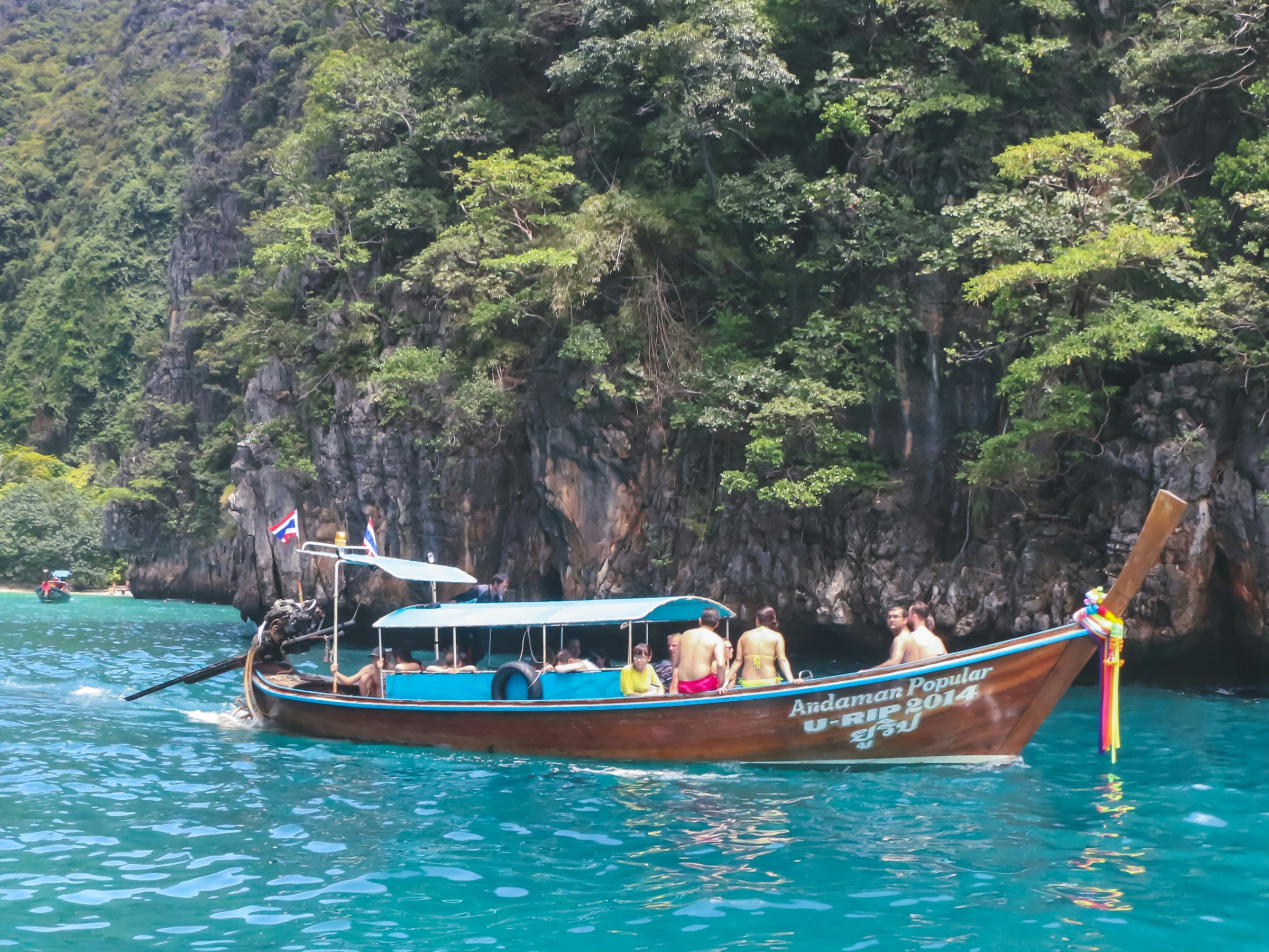 Longtail boat with tourists on turquoise water near lush green cliffs